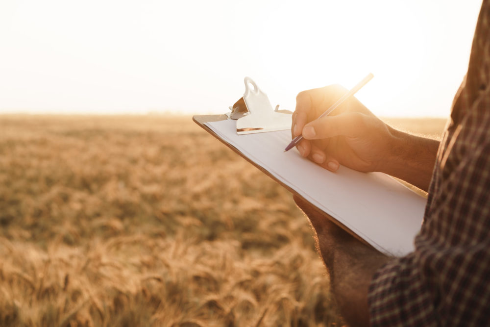 Man taking notes on his clipboard while standing in front of a field